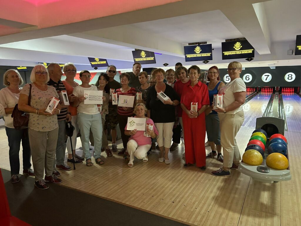 Grupa głównie kobiet pozująca do zdjęcia przy torach oznaczonych numerami 5–8 w kręgielni Magdalena Bala Bowling; wiele z nich trzyma certyfikaty lub niewielkie pudełka; na pierwszym planie widać zwrotnik z kolorowymi kulami, a w tle jasne oświetlenie i ekrany z logo.